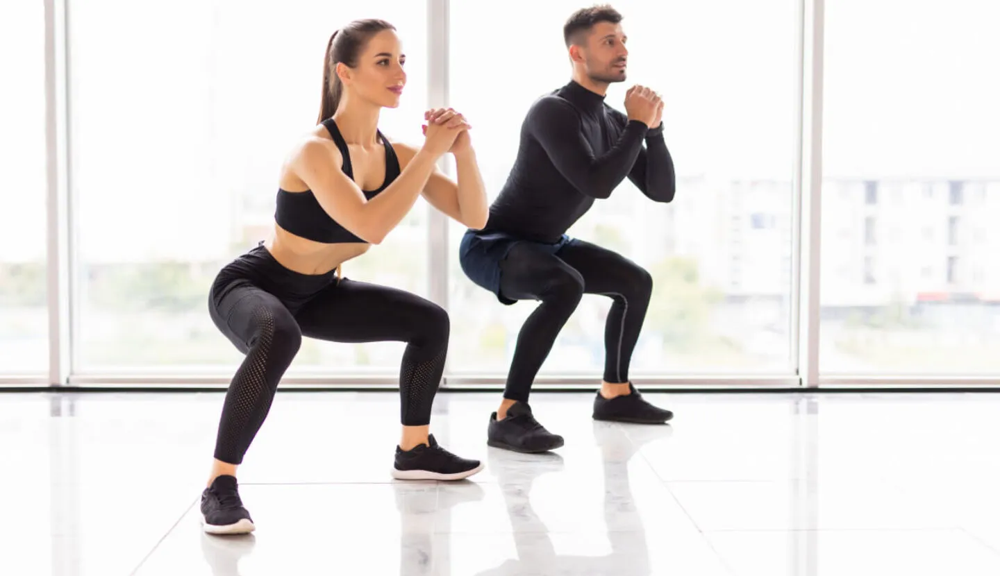 Wspólny trening - Kobieta i mężczyzna wykonujący przysiady podczas treningu siłowego na siłowni FitLife Zamość