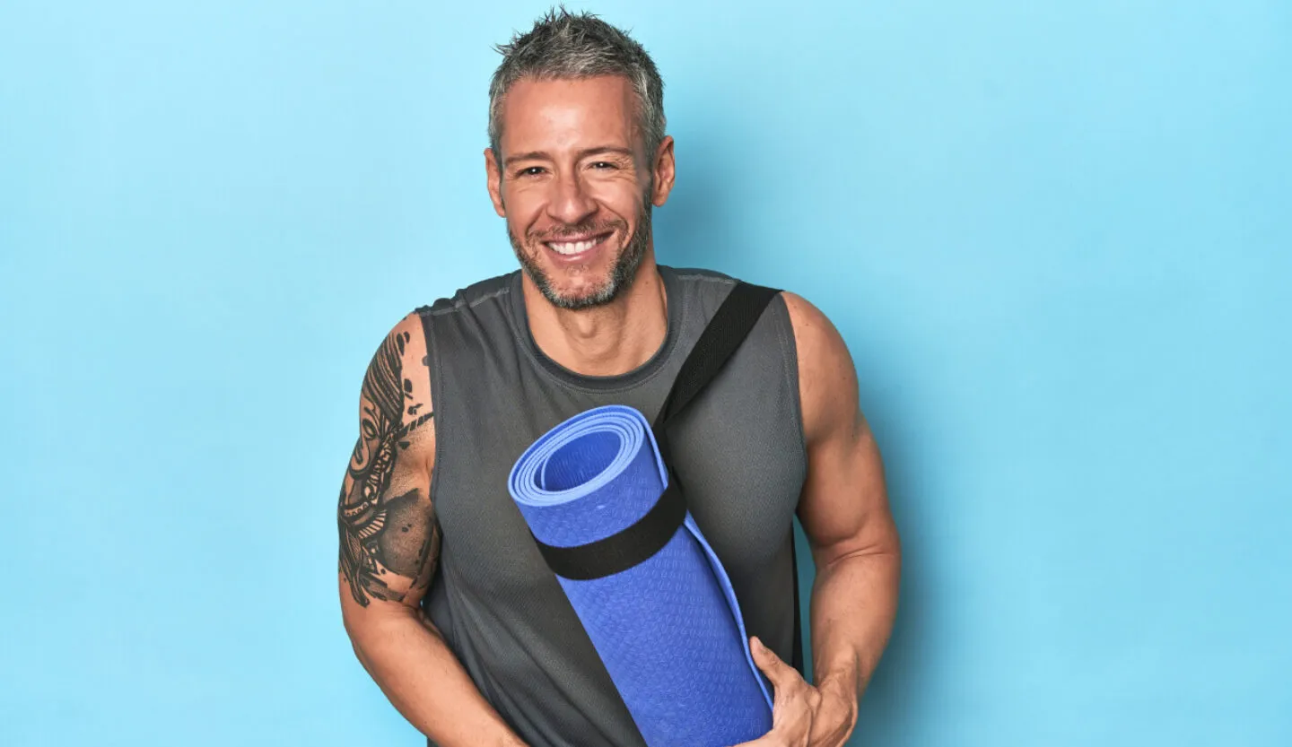 Uśmiechnięty mężczyzna trzyma matę, jest przygotowany do treningu fitness na siłowni FitLife Zamość